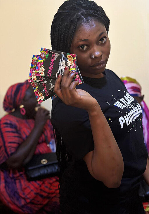 Eine Frau mit drei Frauenkondomen in der Hand blickt selbstbewusst in die Kamera