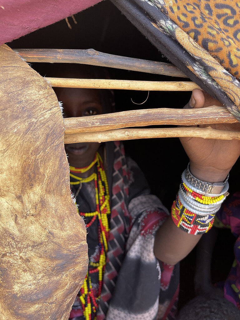 Eine 14-Jährige Kenianerin schaut aus einer kleinen Öffnung ihrer Hütte hinaus, ihr Gesicht ist hinter vier Ästen versteckt und nicht zu erkennen