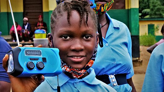 Mit Radiogeräten erhalten auch Gemeinden ohne Strom- und Internetzugang lebenswichtige Informationen zum Umgang mit dem Virus, wie dieses Mädchen aus einer Gemeinnde in Sierra Leone. © Plan International