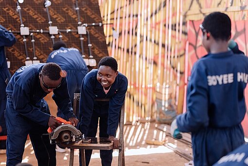 Die Auszubildenden in ihren blauen Uniformen schneiden ein Stück Holz zurecht 