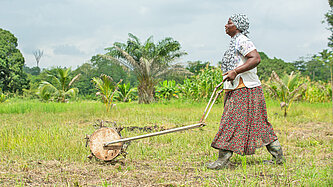 Eine Frau in Arbeitskleidung pflügt mit einer Maschine über ein Feld