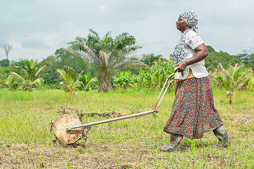 Eine Frau in Arbeitskleidung pflügt mit einer Maschine über ein Feld