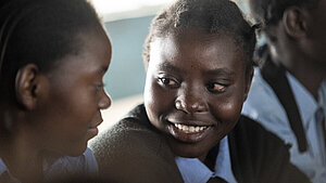 Schülerinnen in Sambia: Bildung als Schlüssel zur Stärkung junger Frauen. Zwei sambische Schülerinnen in Schuluniform sitzen nebeneinander und lächeln sich an – symbolisch für Bildung, Freundschaft und Empowerment junger Frauen.