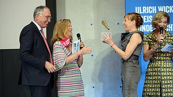 Dr. Werner Bauch, Vorstandsvorsitzender von Plan International Deutschland, und Plan-Patin Marion Kracht überreichen Joanna Michna die Trophäe. Kerstin Straub verliest Glückwünsche an die Gewinnern, die Plan über Twitter erreichen. © Plan / Alexander Schumann