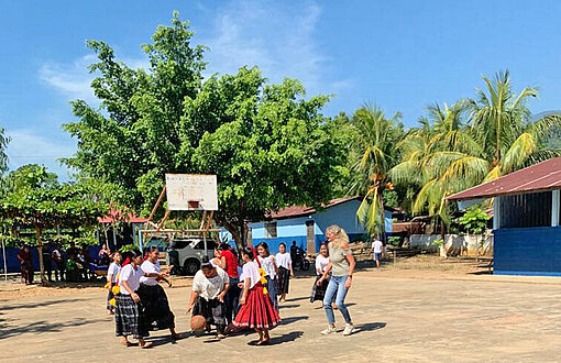 Auf einem sandigen Platz zwischen Palmen spielen mehrere Personen Basketball