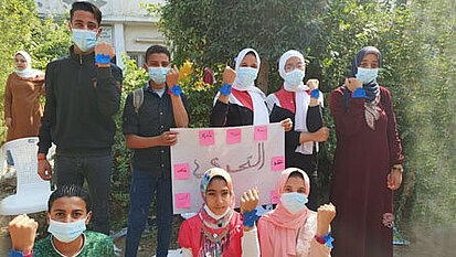 Jugendliche Ägypter:innen halten ein Plakaat in der Hand und zeigen ihre Faust