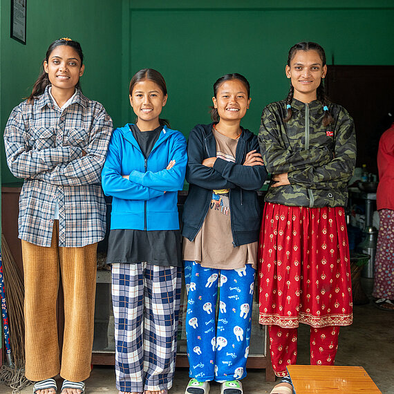 Vier junge Frauen mit Hörbeeinträchtigung aus Nepal stehen nebeneinander im Eingang ihres Snackshops. Die Gruppe nimmt erfolgreich am Jugendförderprogramm teil und betreibt gemeinsam ein inklusives kleines Restaurant.