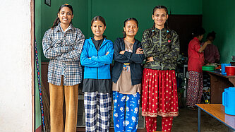 Vier junge Frauen mit Hörbeeinträchtigung aus Nepal stehen nebeneinander im Eingang ihres Snackshops. Die Gruppe nimmt erfolgreich am Jugendförderprogramm teil und betreibt gemeinsam ein inklusives kleines Restaurant.