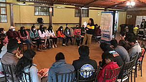 Jugendliche und junge Erwachsene sitzen im Stuhlkreis und nehmen an einem Workshop von Plan International in Ecuador teil. Eine Person steht und moderiert.
