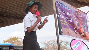 Mädchen in Schuluniform spricht mit Mikrofon auf einer Bühne beim „Tag des afrikanischen Kindes“ in Simbabwe.
