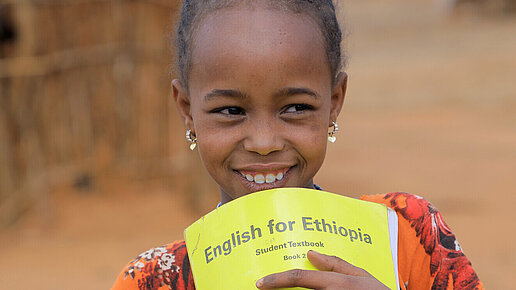 Ein Mädchen hält ein Englisch-Heft in der Hand und lächelt.