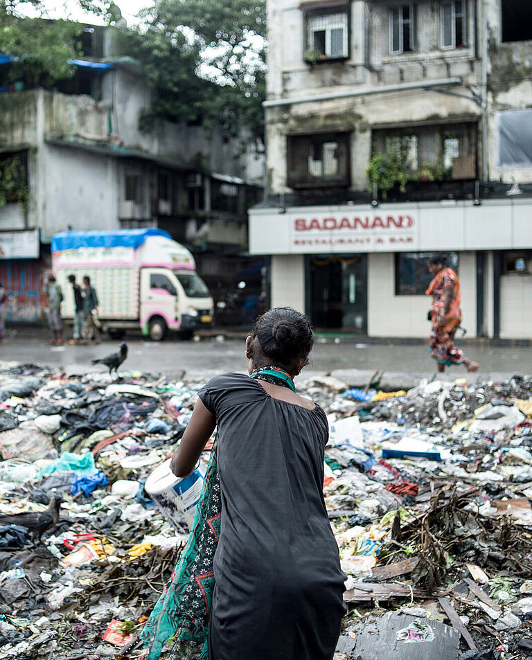 Eine Frau kippt einen Eimer mit Müll auf die Straßen von Mumbai