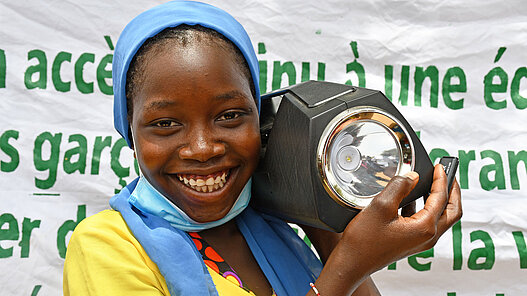 Ein Mädchen aus Niger zeigt stolz ihr tragbares Radio, das sie von Plan International bekommen hat.