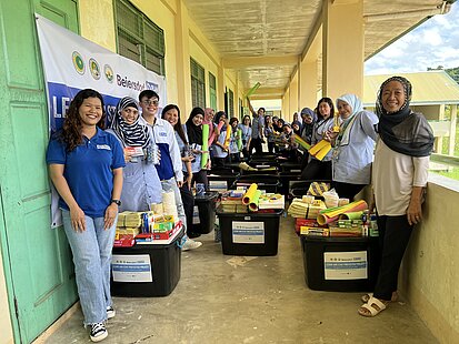 Frauen stehen neben schwarzen Boxen mit Schulmaterialien