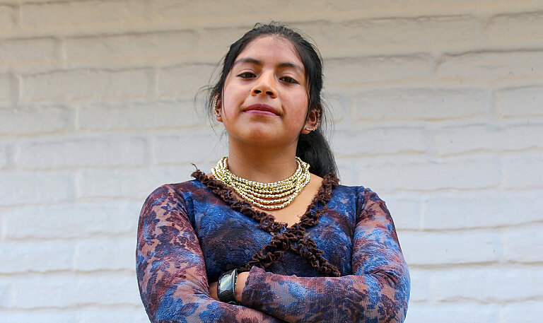 Yadira steht selbstbewusst mit verschränkten Armen vor einer Wand.