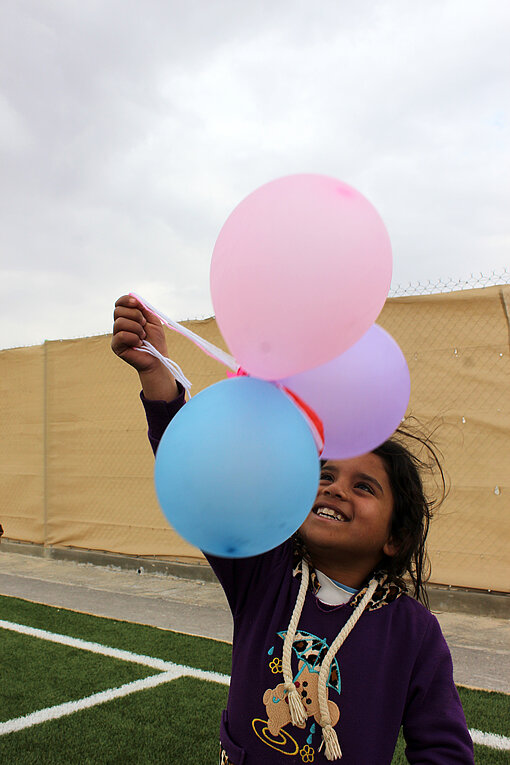 Ein lachendes Mädchen hält ein Bündel aufgeblasener Luftballons in die Höhe.