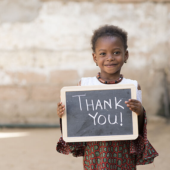 Dankeschön aus dem Senegal: Mädchen bedankt sich mit einem Lächeln für die Unterstützung Mädchen im Senegal hält eine Tafel mit der Aufschrift „Thank You!“ und lächelt in die Kamera