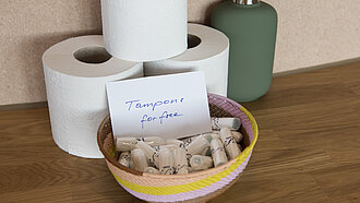 Drei Rollen Toilettenpapier und eine Schüssel mit Tampons
