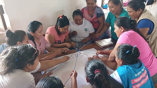 Mehrere Frauen ziehen an Fäden und bewegen gemeinsam einen Stift