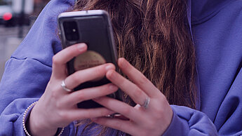 Eine junge Person hält ihr Smartphone in der Hand und ist am Tippen.