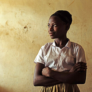 Eine junge Frau steht in einem Raum, sie hat die Arme verschränkt und schaut zur Seite