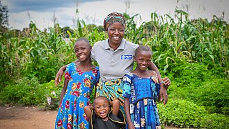 Edwina steht mit drei ihrer Töchter grinsend vor ihrem Maisfeld