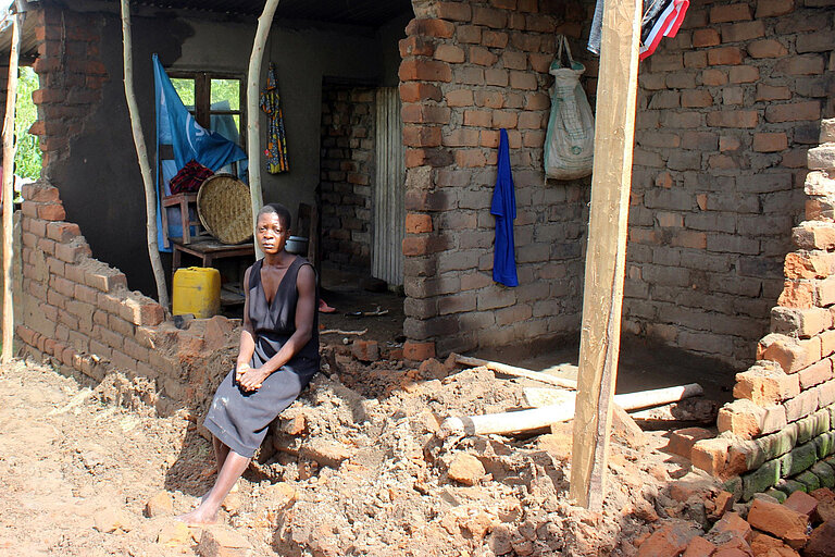 Eine Frau sitzt vor einem zerstörten Haus