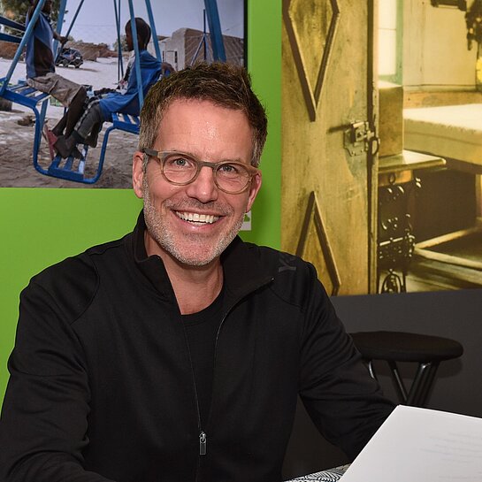 Schauspieler Tim Bergmann sitzt an einem Tisch und hält ein Blatt Papier in der Hand