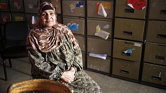 Nagah sitzt auf einem Stuhl vor einem Regal.