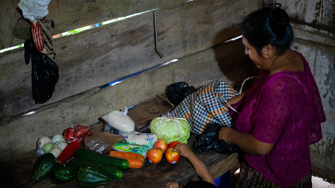 Eine Frau packt in ihrer Küche Gemüse aus. Ein Junge streckt den Arm nach den Äpfeln aus