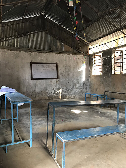 Das Bild zeigt ein leeres Klassenzimmer in Nepal. Man sieht drei Schulbänke und eine Tafel.