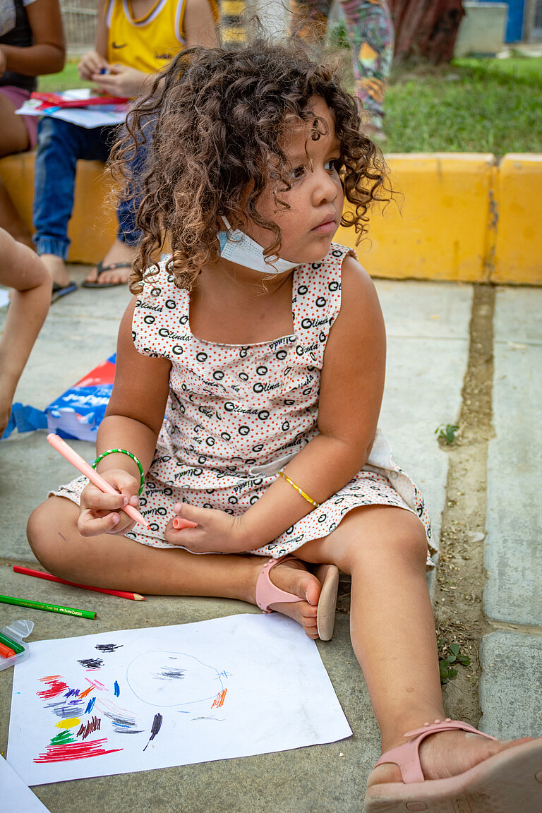 Ein kleines Mädchen sitzt auf dem Boden und malt mit bunten Stiften.