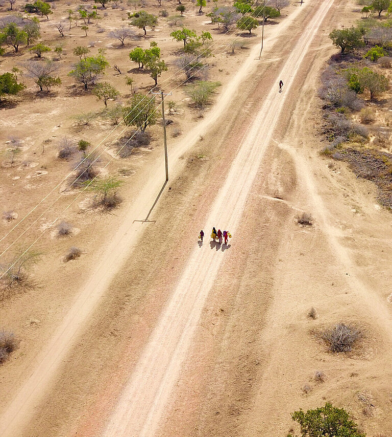 Eine weite, trockene Landschaft von oben, auf einer sandigen Straße laufen vereinzelt Menschen