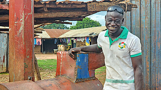 Ein schwarzer junger Mann lehnt lächelnd und lässig an einem Metallamboss