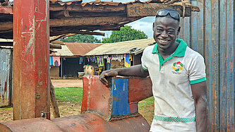 Ein schwarzer junger Mann lehnt lächelnd und lässig an einem Metallamboss