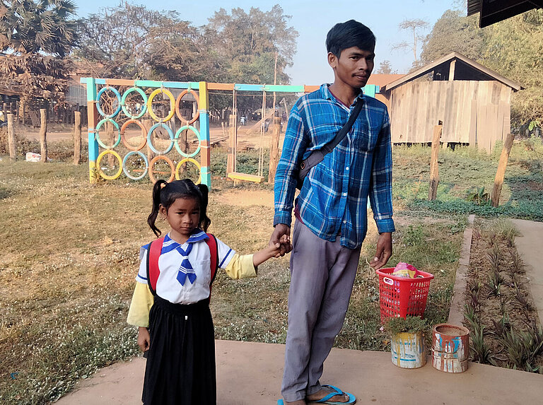 Ein Vater hält seine Tochter an der Hand. Sie trägt eine Vorschuluniform.
