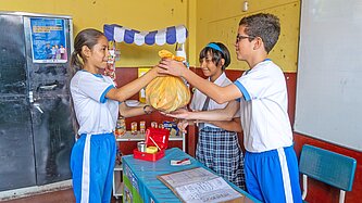 Ein Mädchen in Sportkleidung übergibt eine braune Tüte voller recycelter Abfälle an einen Jungen ebenfalls mit einer Sporthose