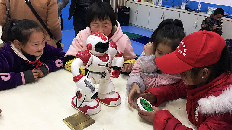 Vier Mädchen spielen mit einem kleinen Roboter.