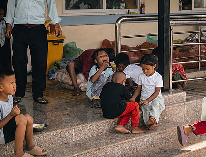 Mehrere Kinder sitzen auf einer Treppe und essen vor einem Gebäude in Nepal, im Umfeld von Nothilfe-Maßnahmen.