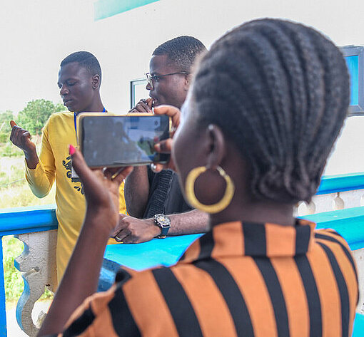 Germaine mit einem Handy in der Hand haltend filmt ein Geschehen