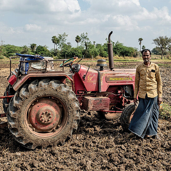 Ein Landwirt steht vor einem Traktor auf einem ausgetrockneten Feld