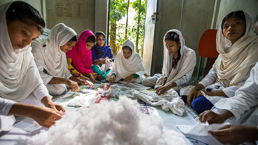 Die veredelte Baumwolle wird gerollt und mit medizinischer Watte geschichtet. Anschließend decken die Mädchen sie mit einem Netzgewebe ab und schneiden sie in die richtige Form. © Plan International