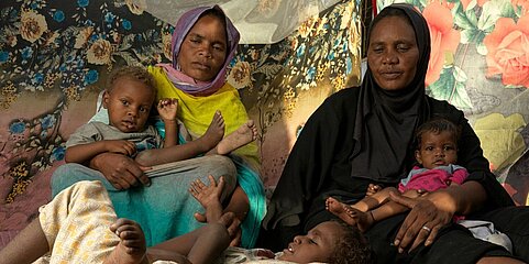 Eine Frau mit ihren Kindern, von denen zwei (liegend) mit Behinderung leben.