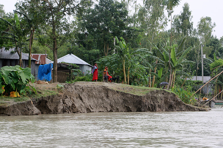 Ein abgebrochenes Ufer, direkt dahinter steht ein Haus, davor sieht man Hochwasser