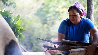 Bäckerin in Honduras legt Feuerholz für Lehmofen nach