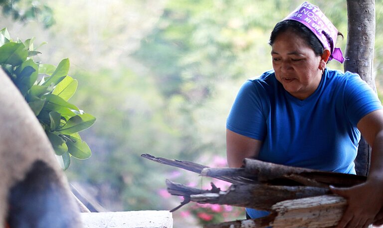 Bäckerin in Honduras legt Feuerholz für Lehmofen nach