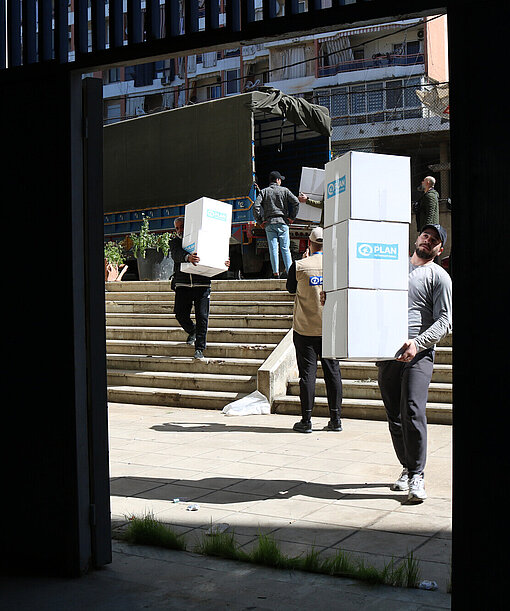 Mehrere Männer tragen Kisten mit Hilfsgütern von Plan International in ein Gebäude