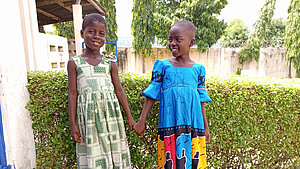 Freundschaft und Bildung in Togo – Mädchen halten sich an den Händen Zwei Mädchen in bunten Kleidern halten sich an den Händen und lächeln – Aufnahme in einer Schule in Togo.