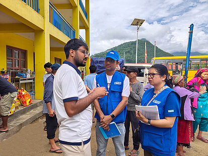Mitarbeiter von Plan International im Austausch mit Gemeindemitgliedern bei einer Nothilfeaktion vor einem gelben Gebäude in Nepal.