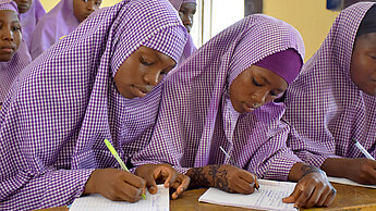 Mädchen sitzen in einem Klassenzimmer und schreiben in ihre Hefte